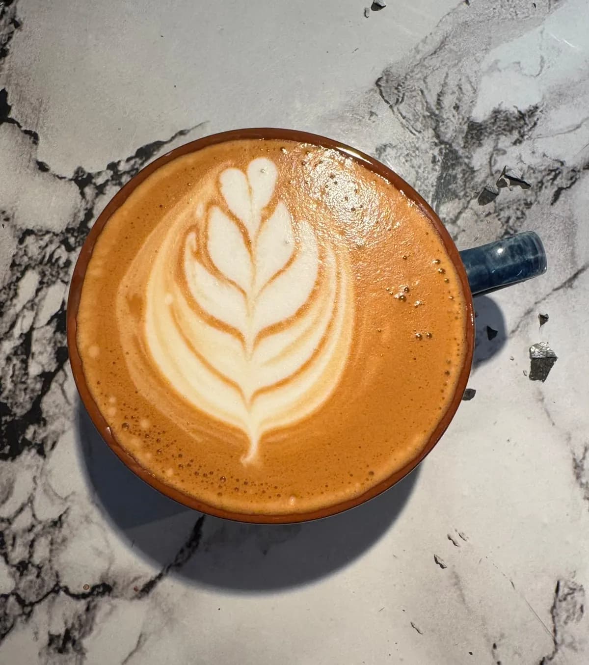 A latte with a rosetta poured into it, seen from above on a marble table.