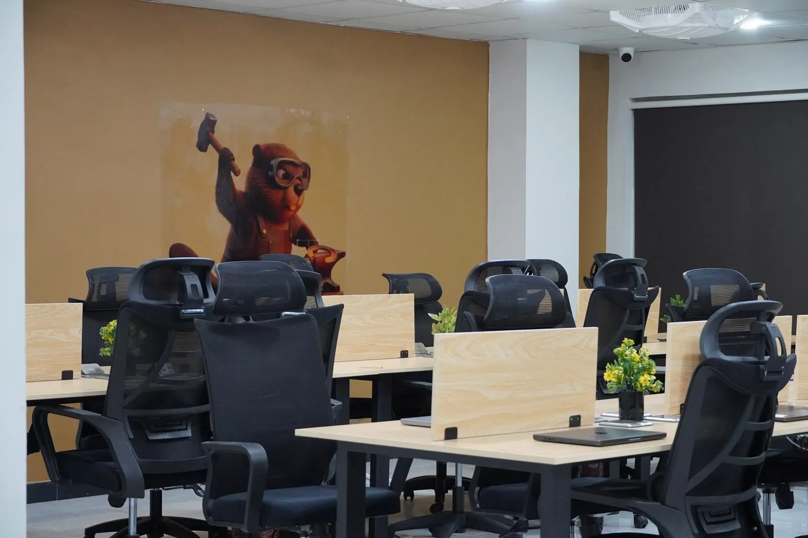 Rows of desks and black office chairs under a mural of a beaver swinging a hammer.