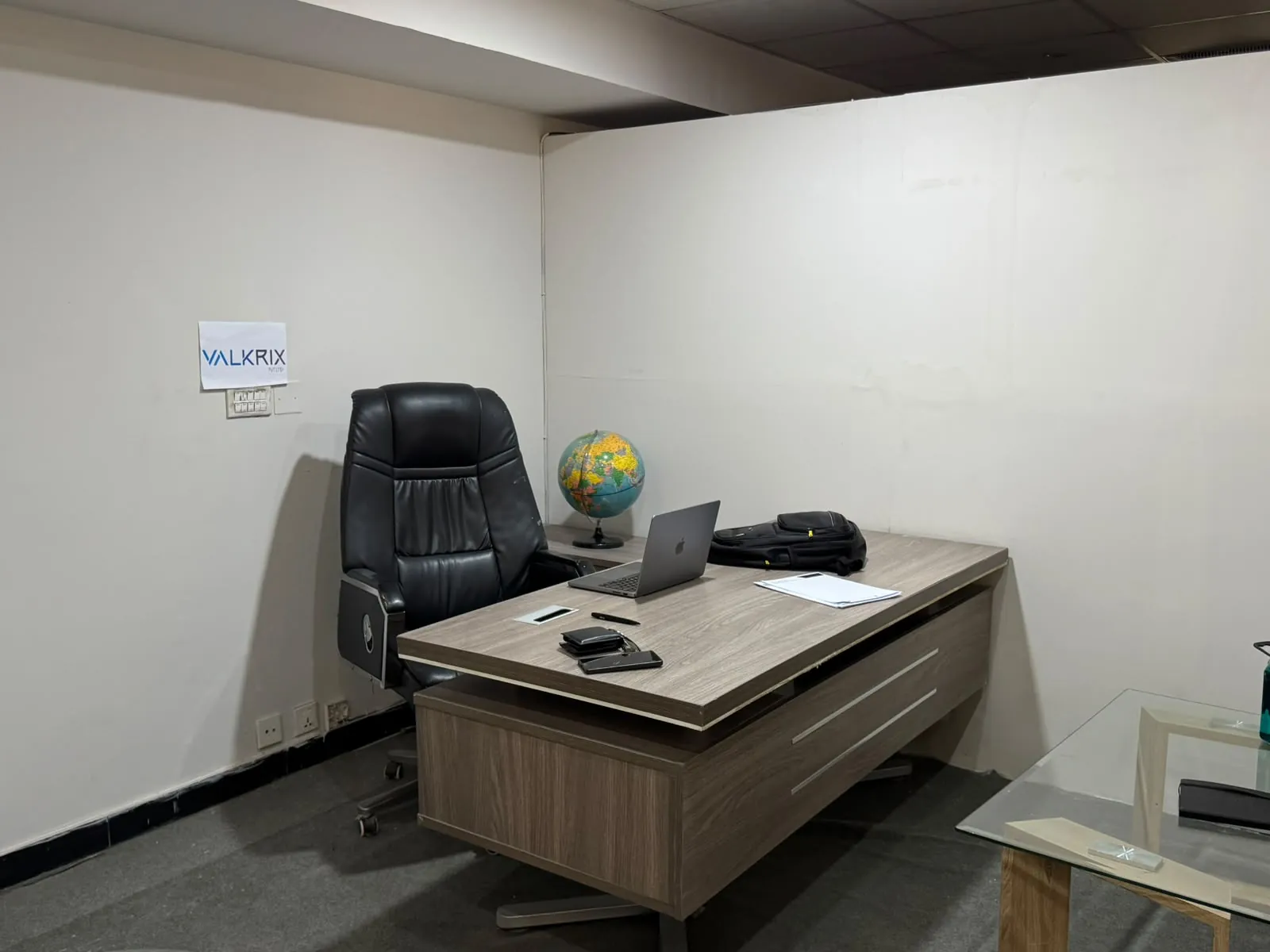 A desk with a laptop and a globe in an office, with a Valkrix sign on the wall behind it.